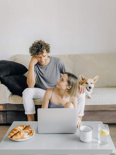 Young couple with their dog and a laptop on the sofa in the living room
