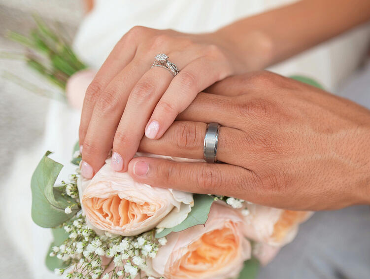 Hands with wedding rings resting on a bouquet