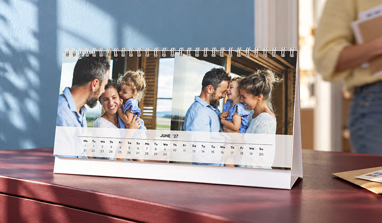 A spiral-bound desk calendar with family photos on a red table