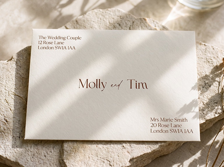 Cream envelope on a stone slab, printed with the couple's names, sender address top left and recipient bottom right