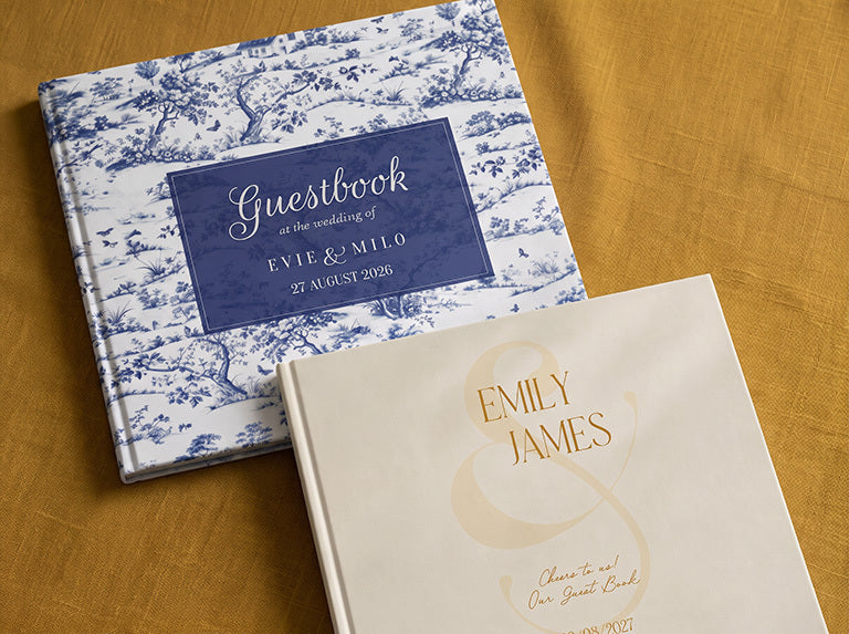 Two wedding guest books with names and date on the cover: blue-and-white toile, and cream with gold lettering