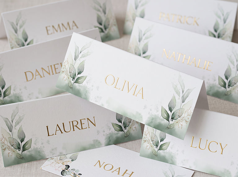 Tent place cards with a green leaf design, each printed with a different guest name in gold foil