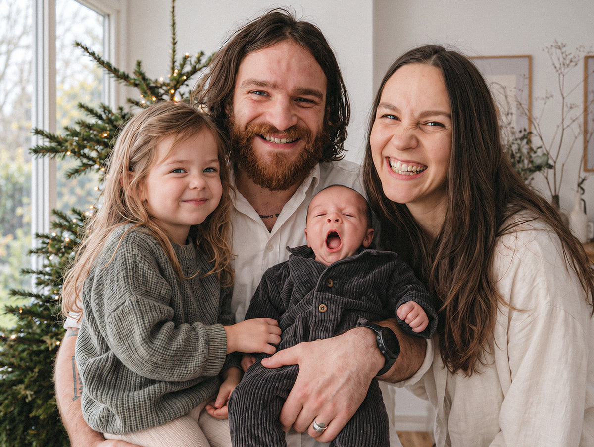 A young family with their newborn baby in front of a Christmas tree