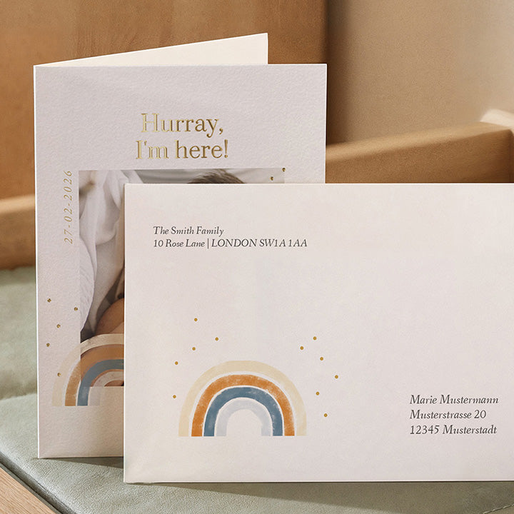 A birth card with a rainbow design in front of its matching envelope