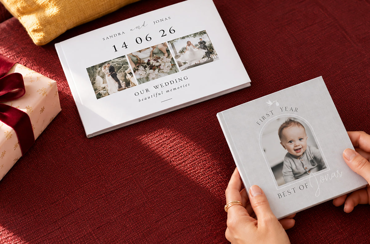 A wedding photo book and a baby's first-year photo book on a red sofa beside a Christmas present
