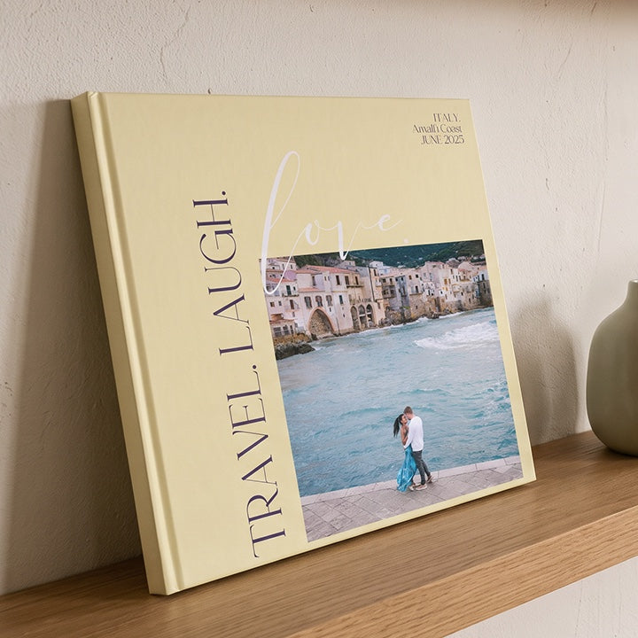 A yellow holiday photo book with a seaside photo, leaning on a shelf