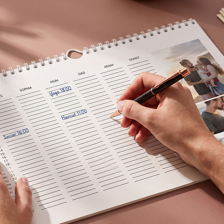 A hand writing appointments into a family calendar with a column for each person