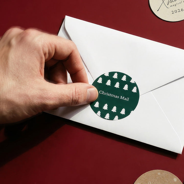 A hand placing a Christmas Mail seal on a white envelope
